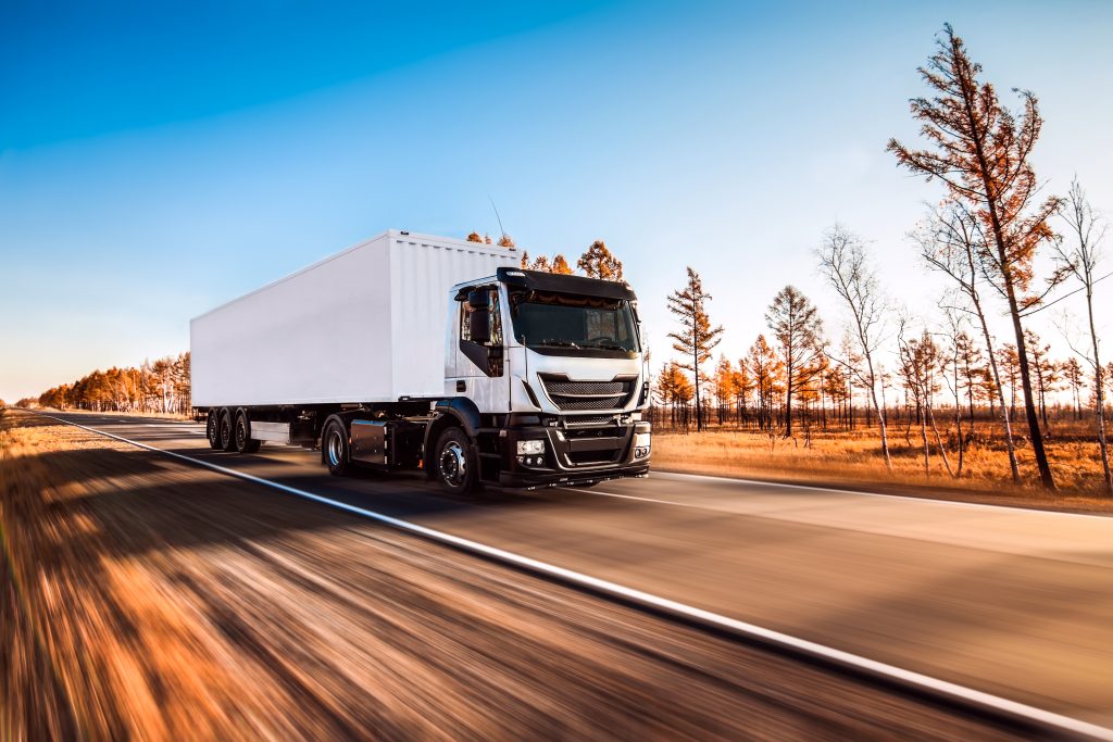 White truck with white trailer on the road in autumn